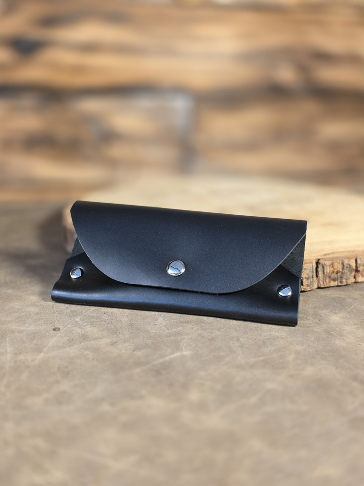 Black leather sunglass case with silver rivets resting against a wooden surface