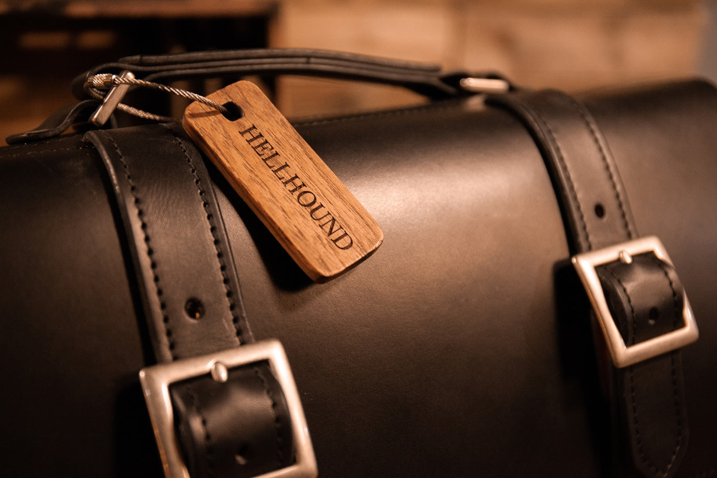 Black leather bag with a wooden tag labeled 'Hellhound' on a blurred background