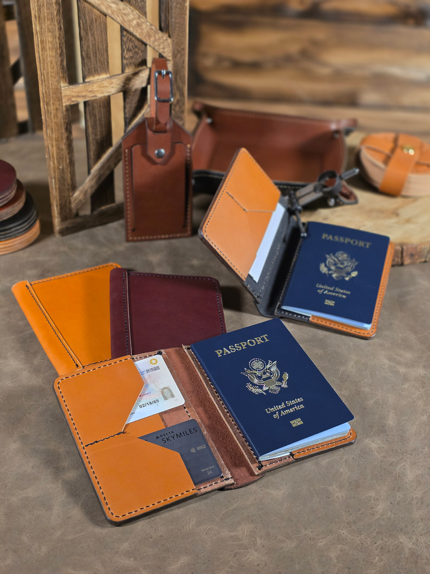 Collection of leather passport holders displaying passports inside on a wooden surface with a variety of leather travel items in the background.
