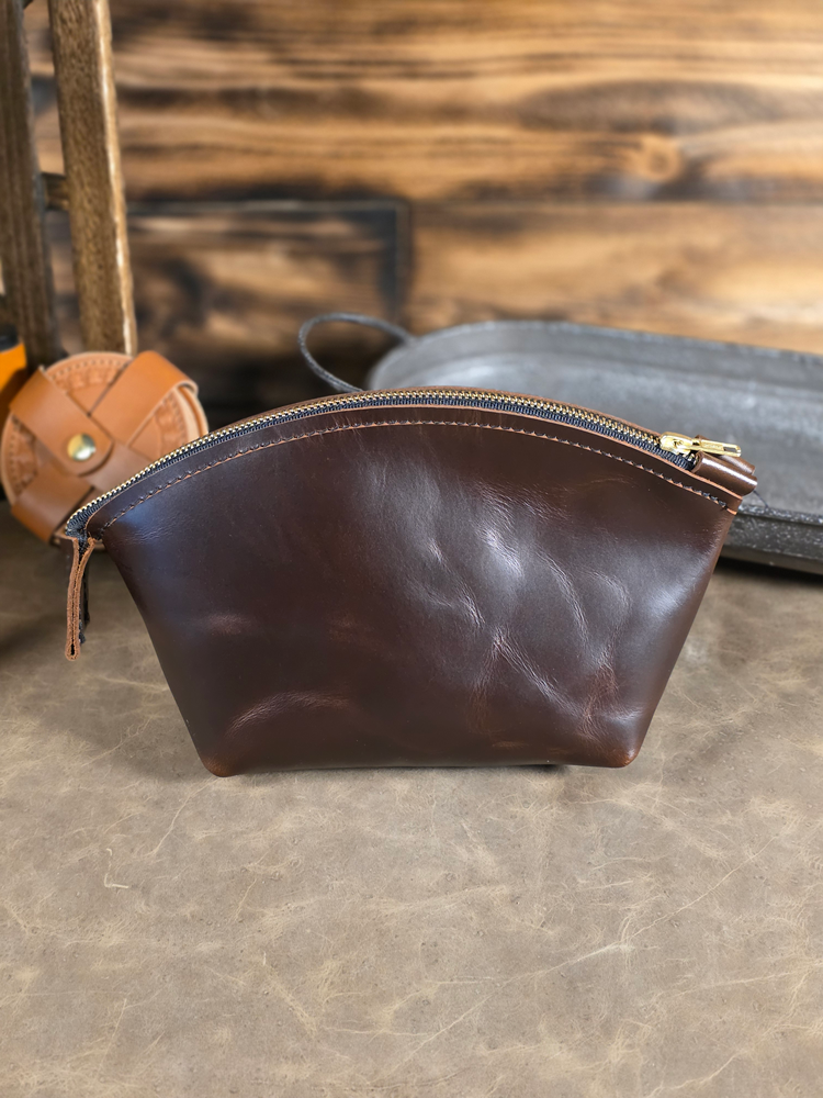 Chocolate brown leather pouch with gold zipper on a textured surface
