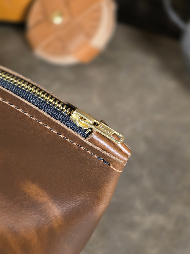 Close-up of a brown leather pouch with a heavy duty solid brass zipper on a blurred background