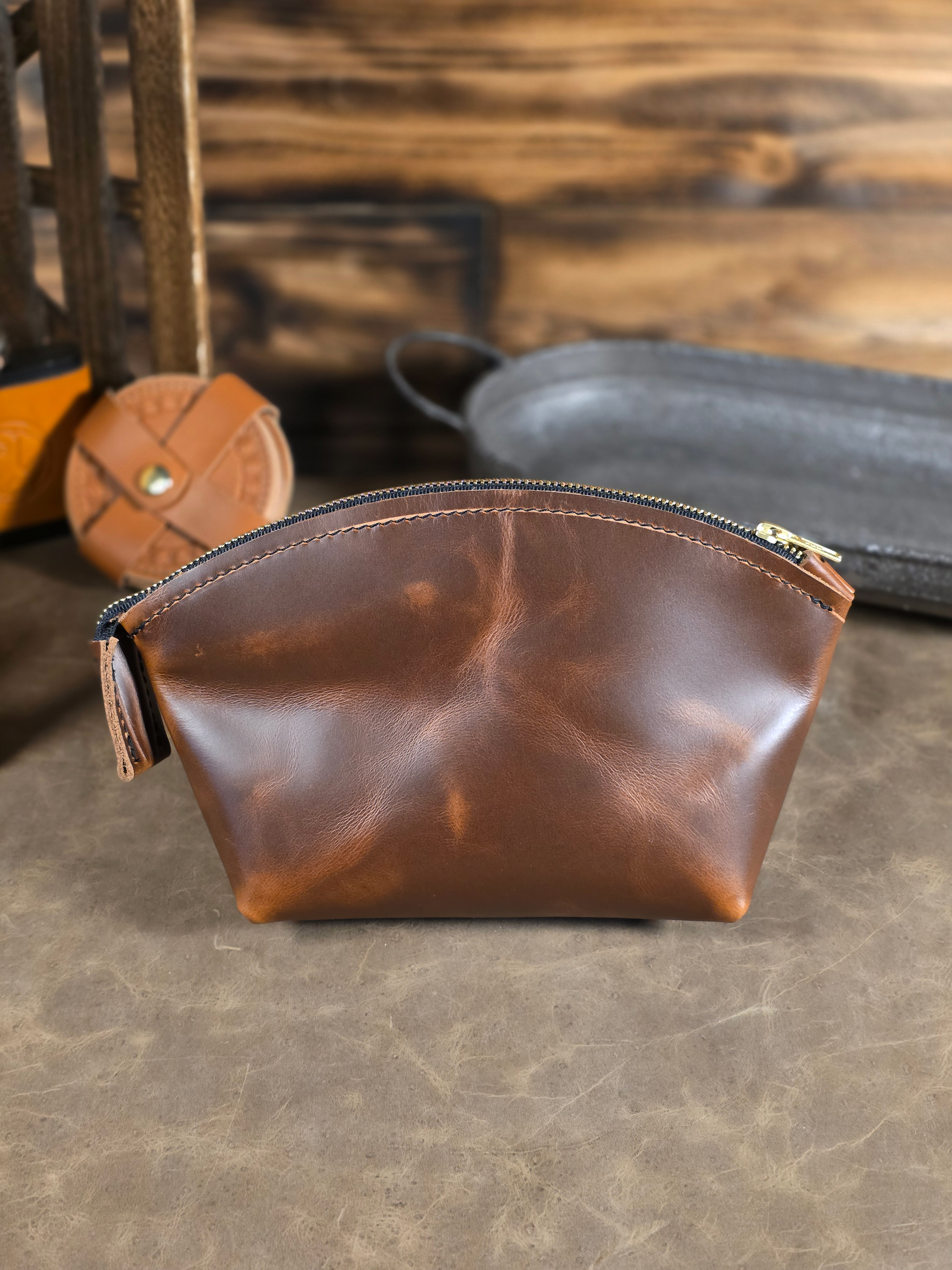 Brown leather cosmetics pouch on a wooden surface with blurred background