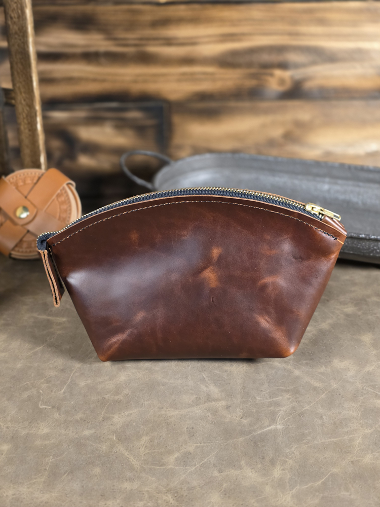 Brown leather pouch with gold zipper on a wooden surface