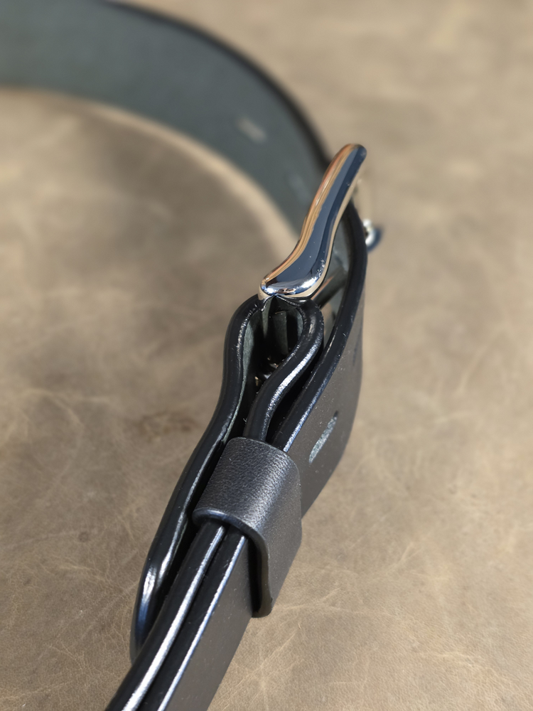 Close-up of a black leather belt with a silver buckle on a beige surface