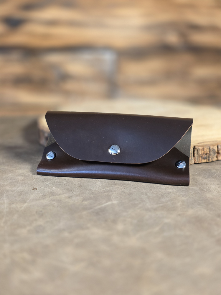 Brown leather wallet with silver buttons on a wooden surface