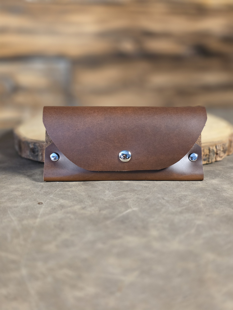 Soft leather sunglass case rests against a wooden plank in cognac brown.