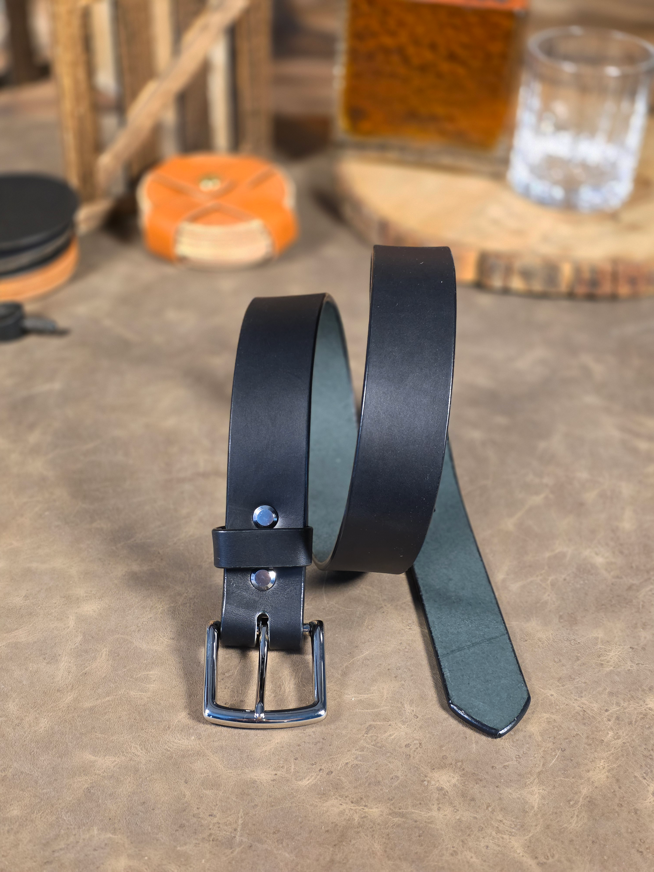 Black leather belt with a silver buckle on a textured surface.