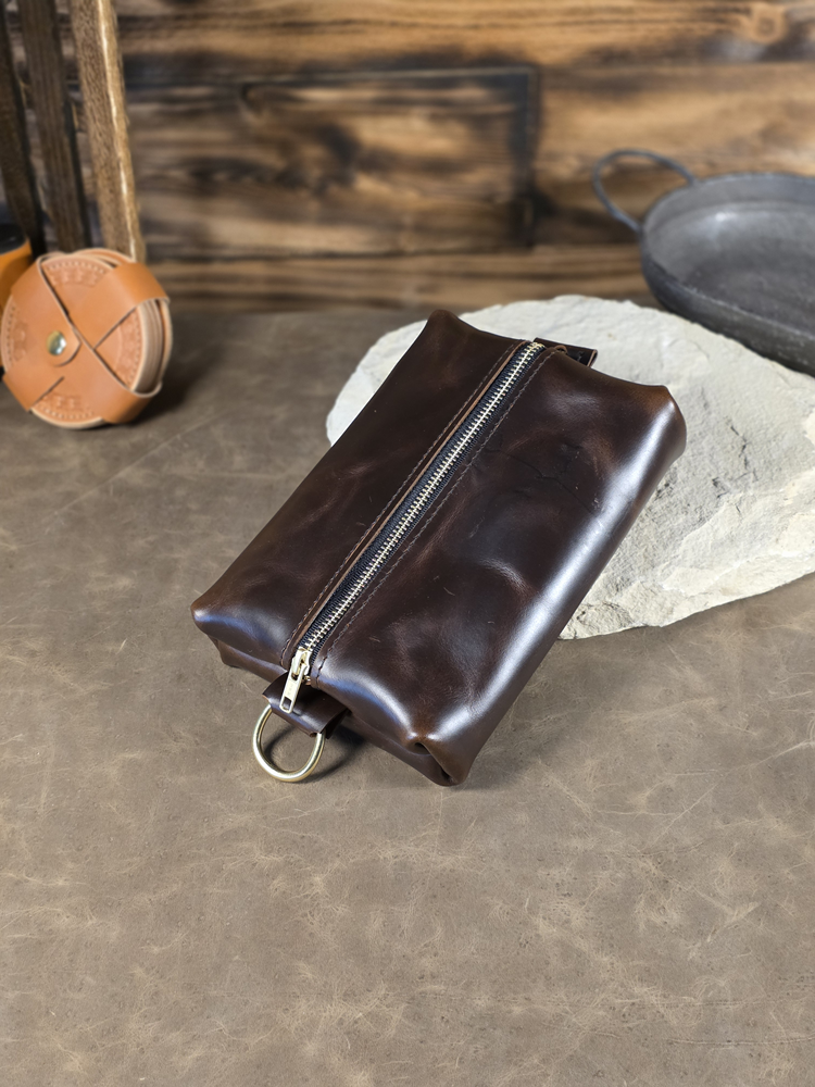 Chocolate brown leather pouch with a zipper on a stone surface with a rustic background