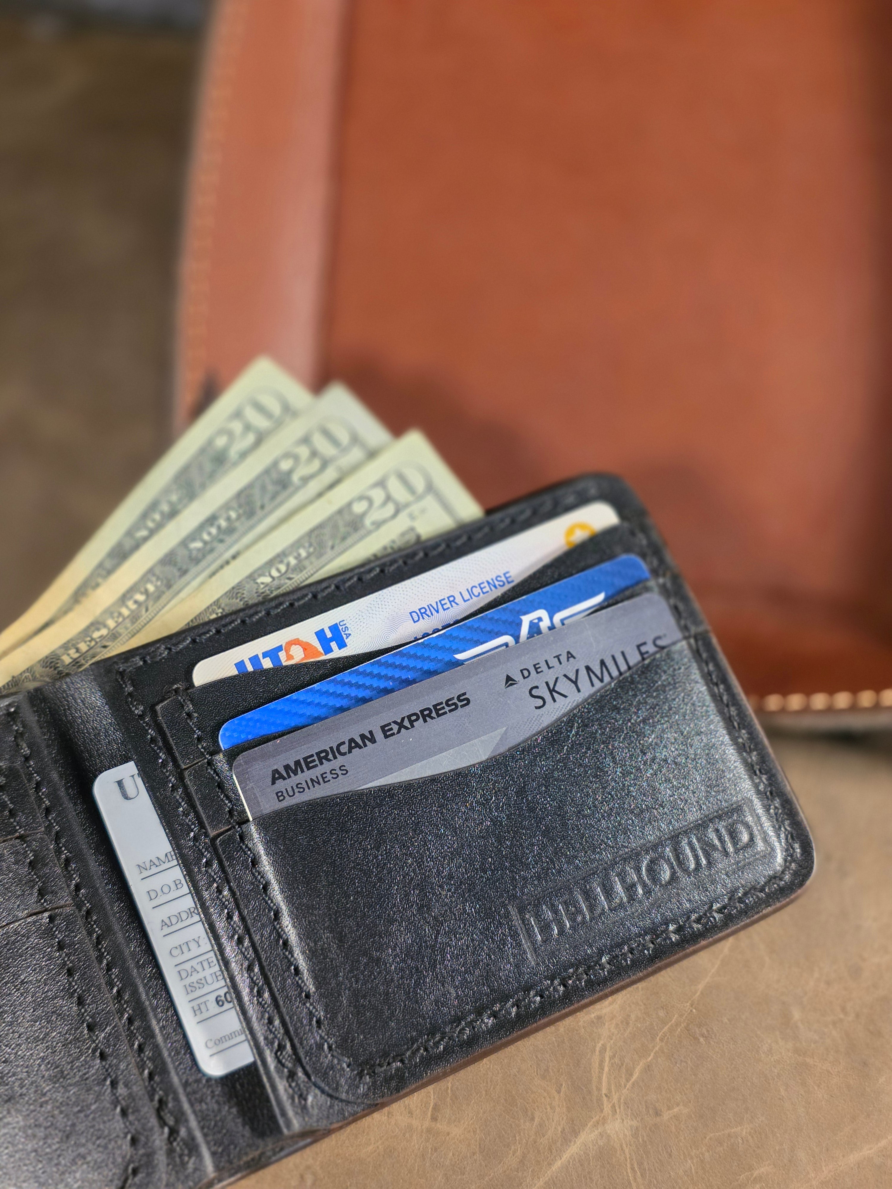 Black leather wallet with cards and money on a brown leather surface