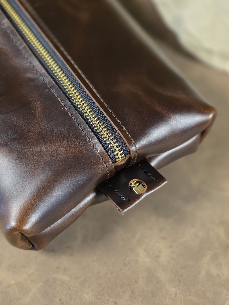 Close-up of a brown leather pouch with a zipper on a beige surface