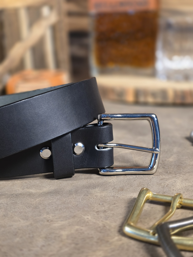 Black belt with silver buckle on a wooden surface, with another belt and gold buckle in the foreground.
