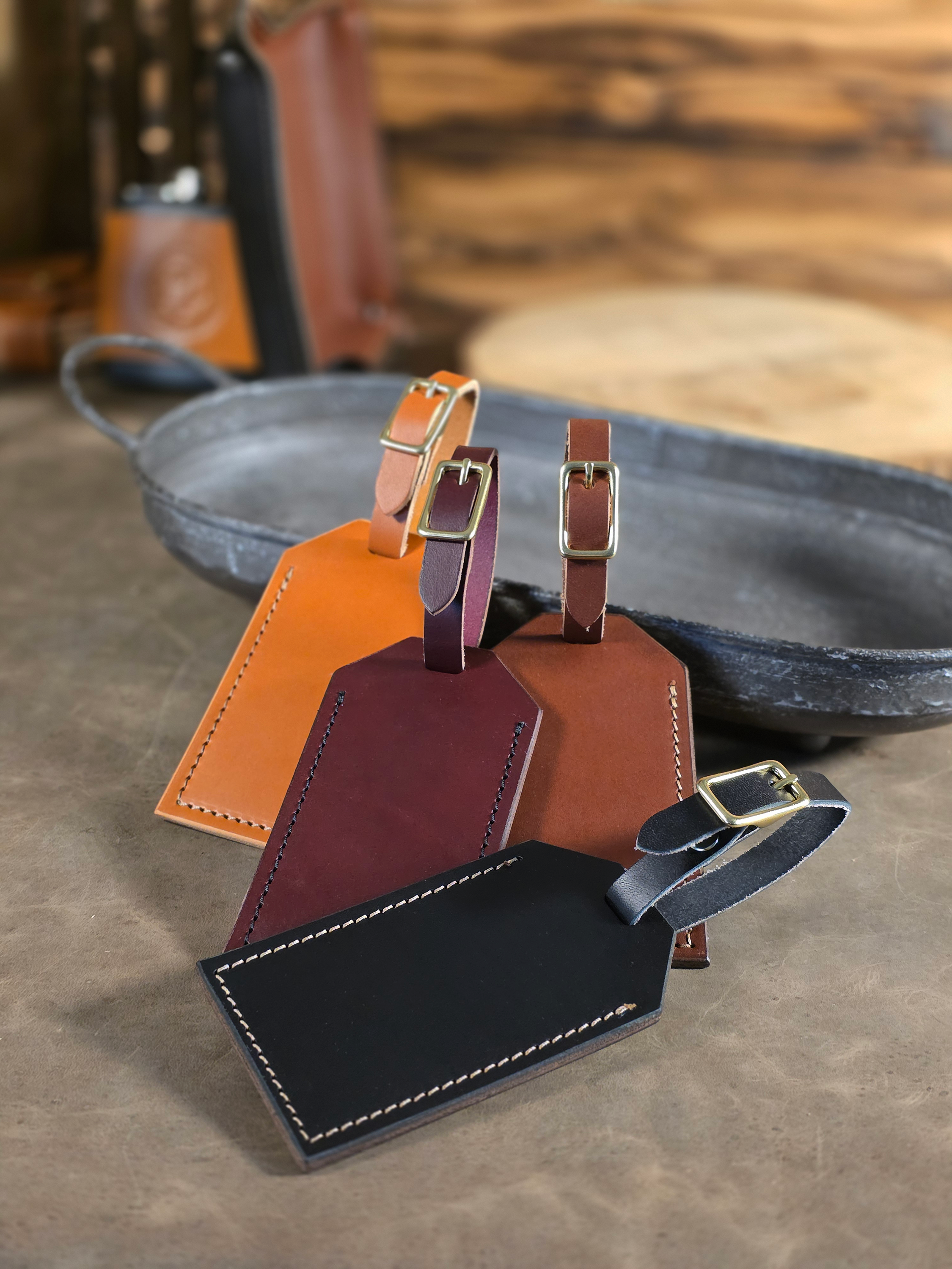 Four leather luggage tags in black, brown, tan and oxblood resting against a metal tray.