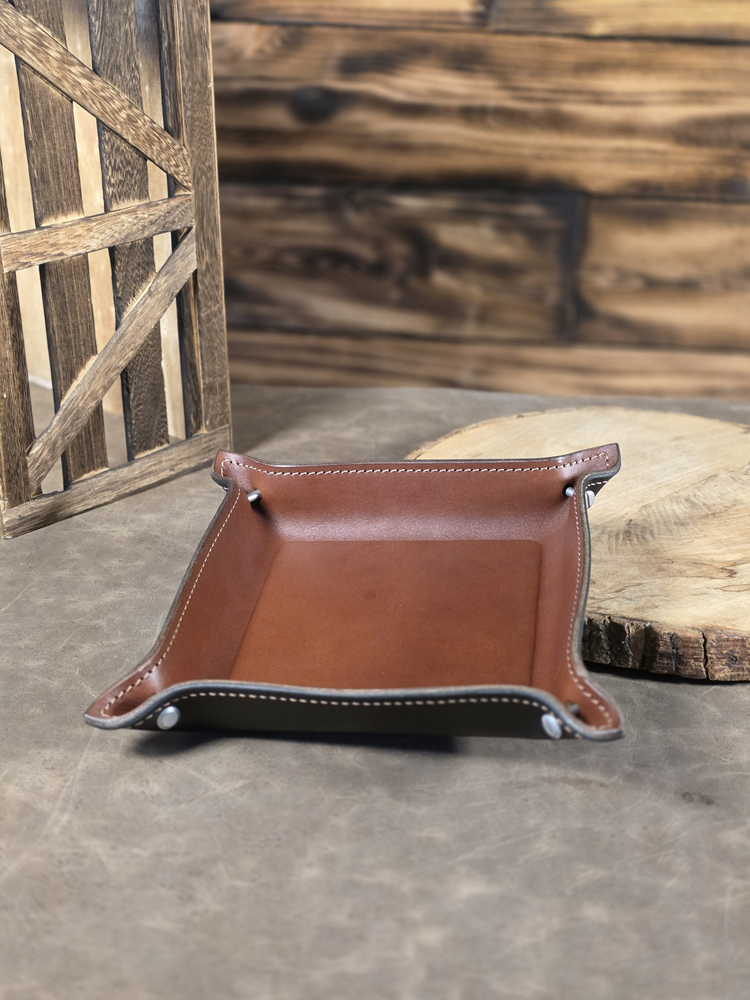 Brown and black leather tray with contrast stitching on a wooden surface