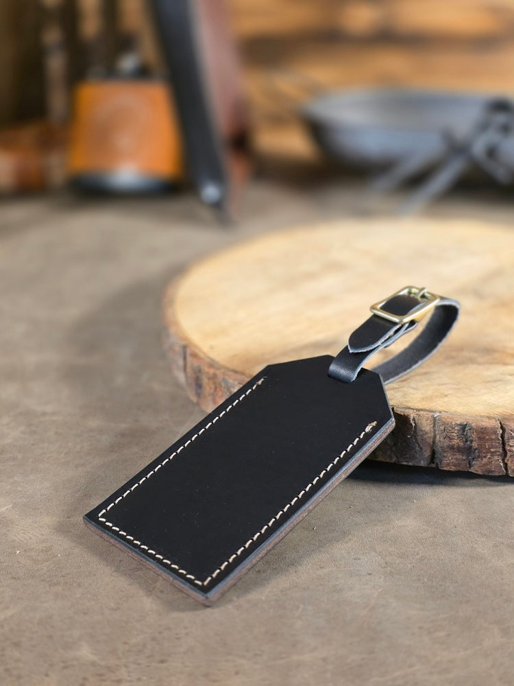 Black leather luggage tag on a wooden surface with a blurred background