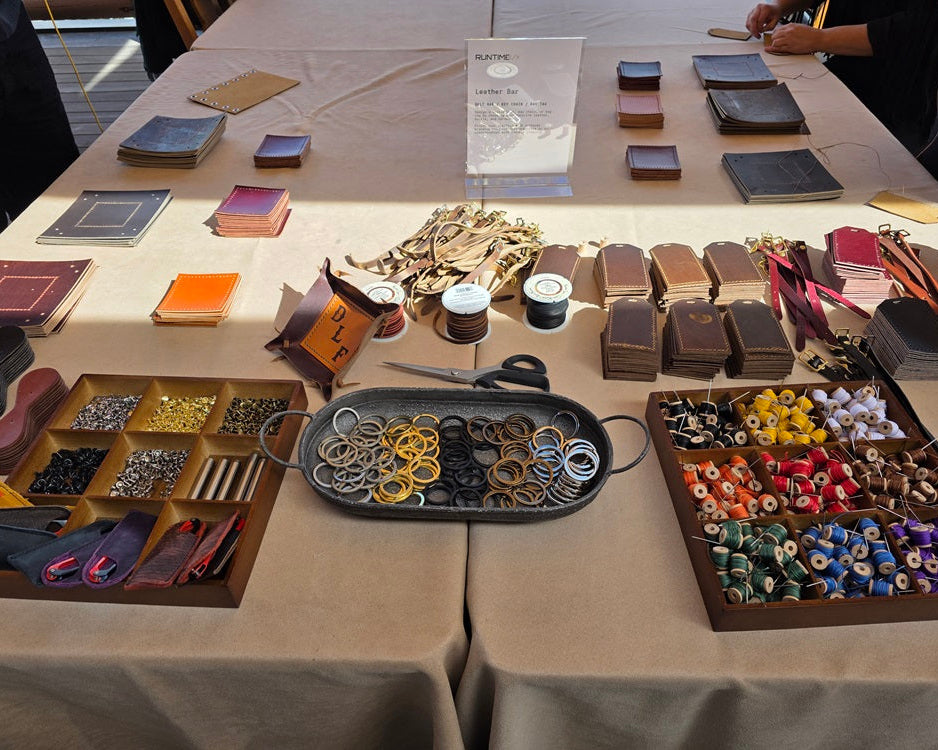 A large collection of colorful leather supplies, leather pieces, bright thread colors, tools and hardware are arranged on a table.