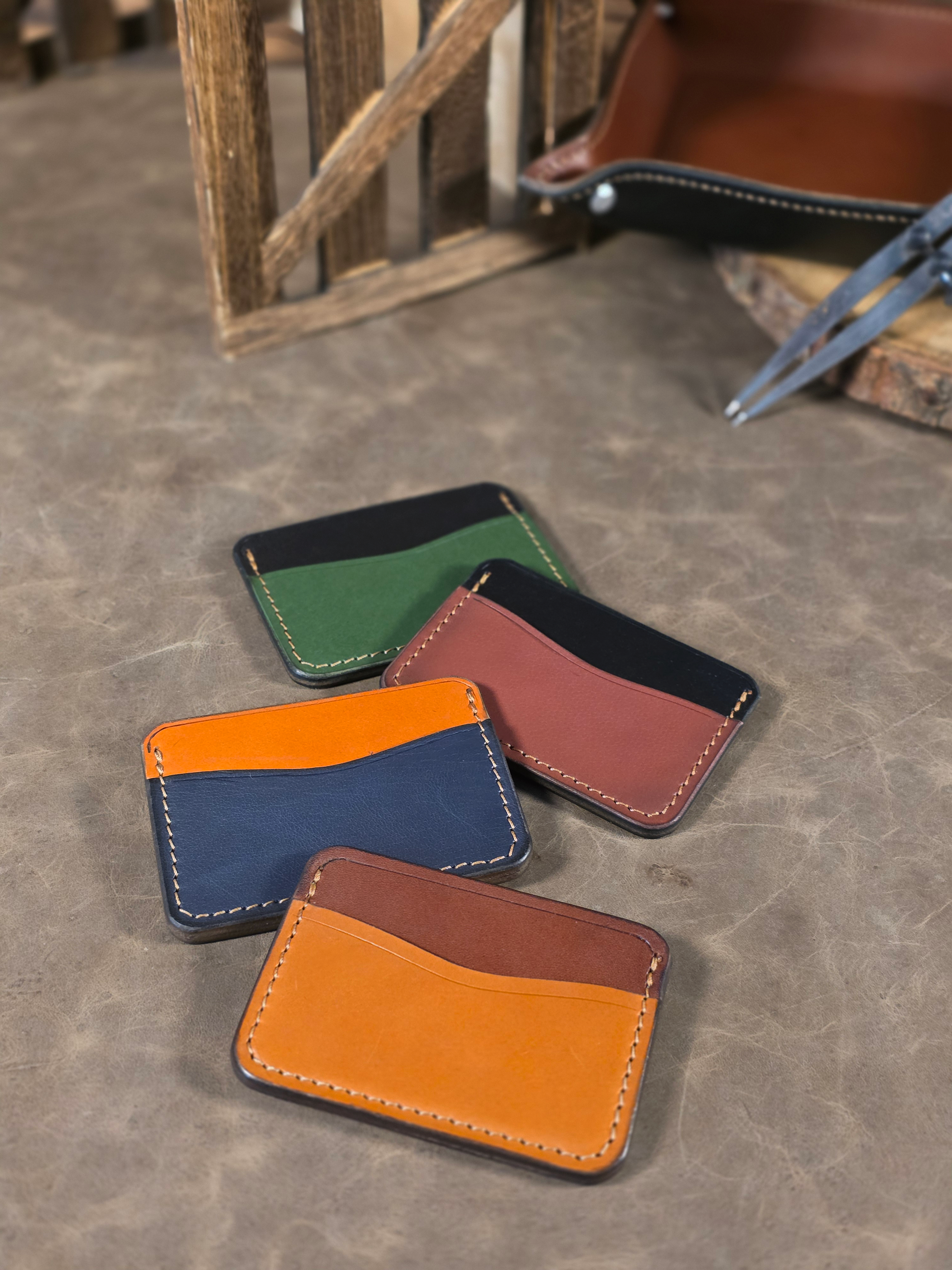 Four leather card holders in different colors on a textured surface.