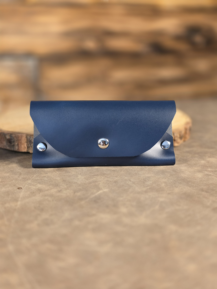 Navy blue leather sunglass case with silver buttons on a wooden surface