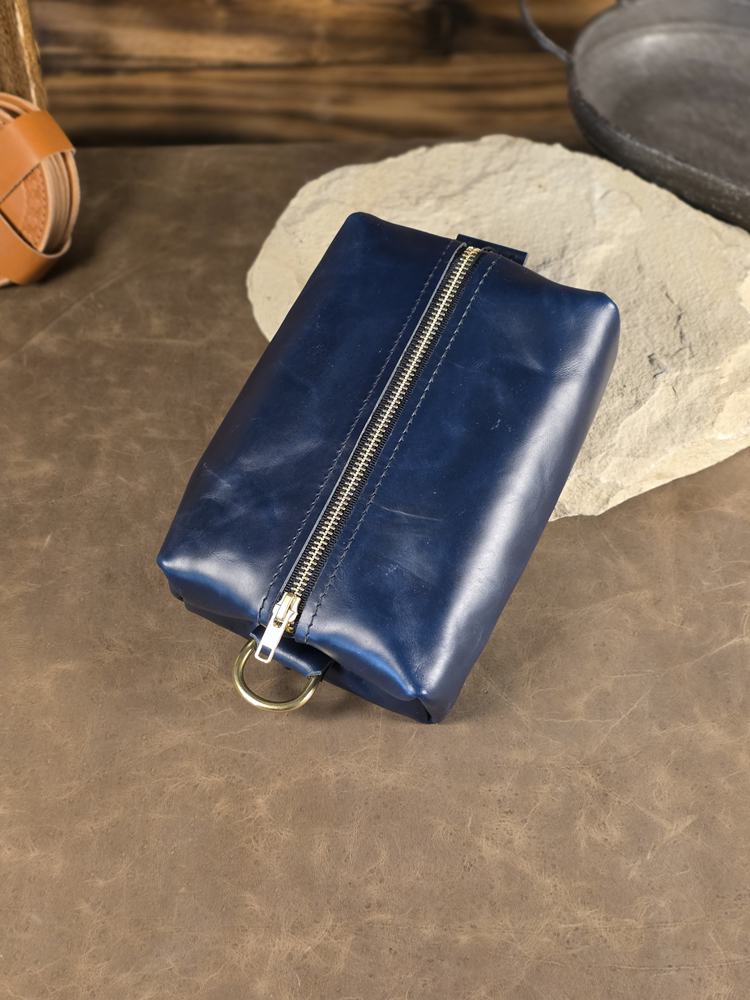 Blue leather pouch with a golden brass zipper resting against a stone surface