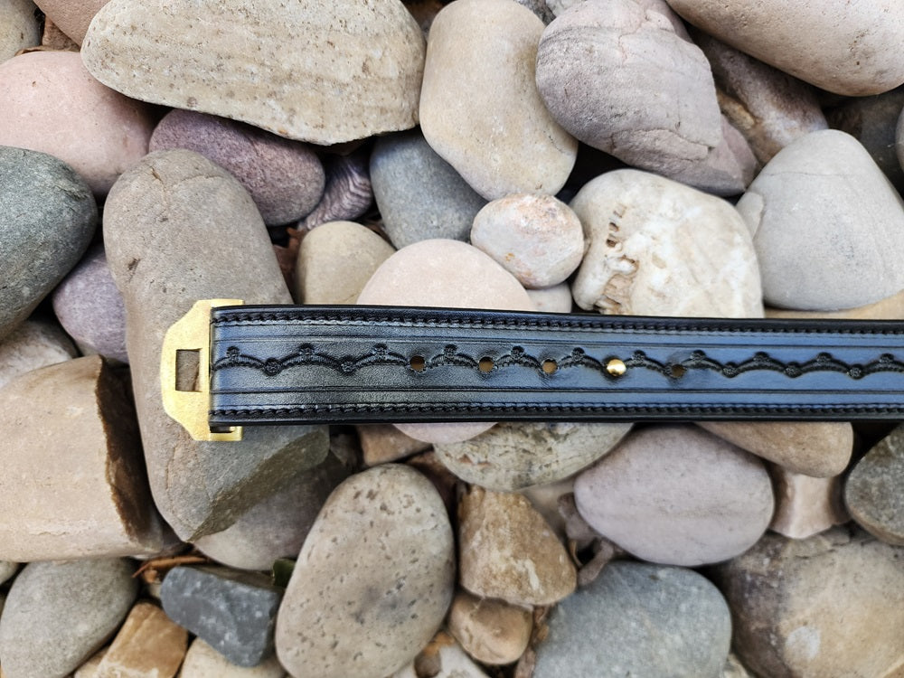 Close up of the rear end of a tooled black belt sitting on pale river rocks.