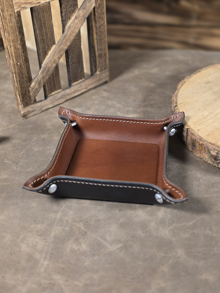 Brown leather tray with black trim on a concrete surface