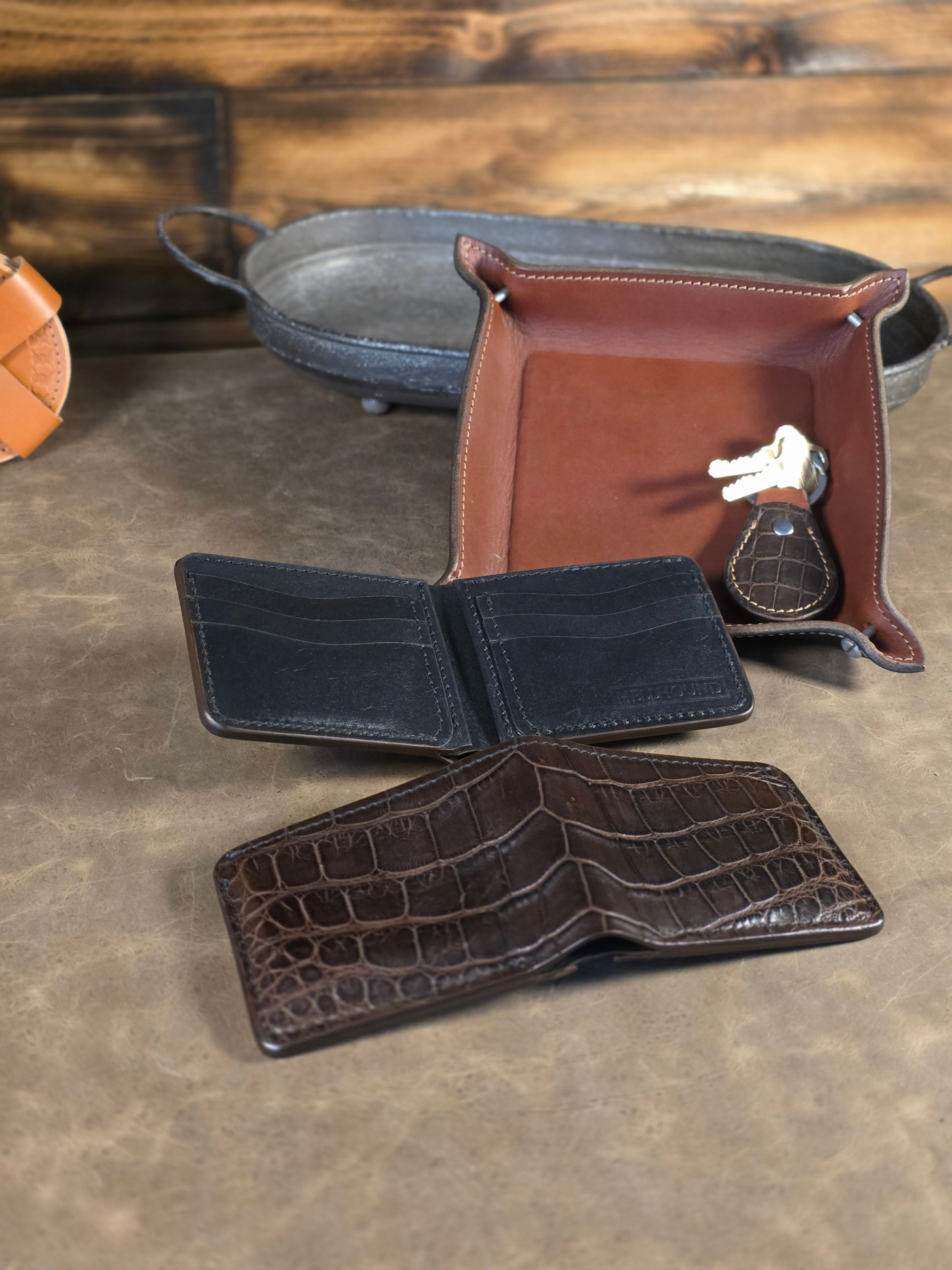 Two wallets, one showing the exterior, one showing the interior, sitting together against a leather valet tray, on a brown leather surface.