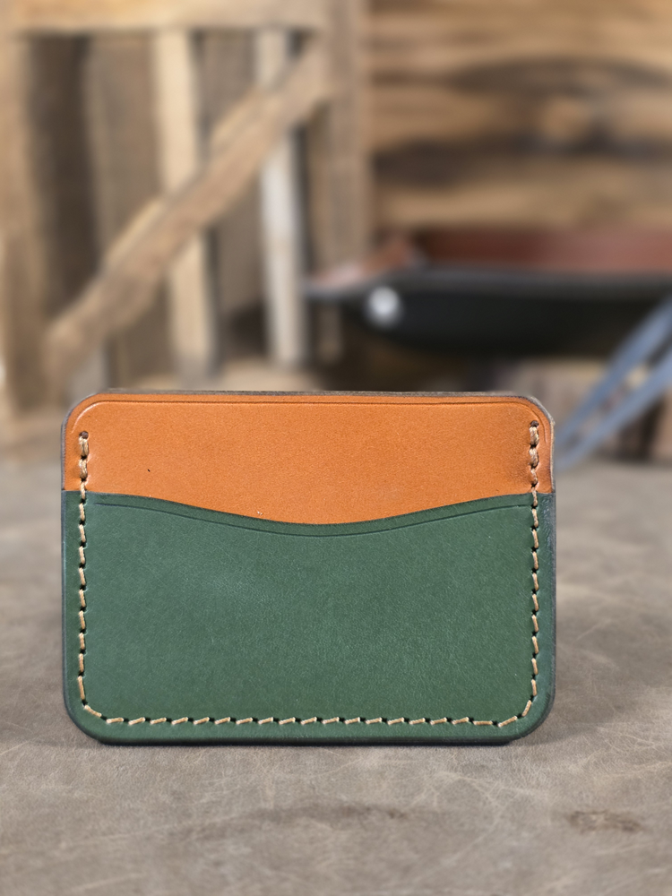 Green and brown leather cardholder on a wooden surface with blurred background