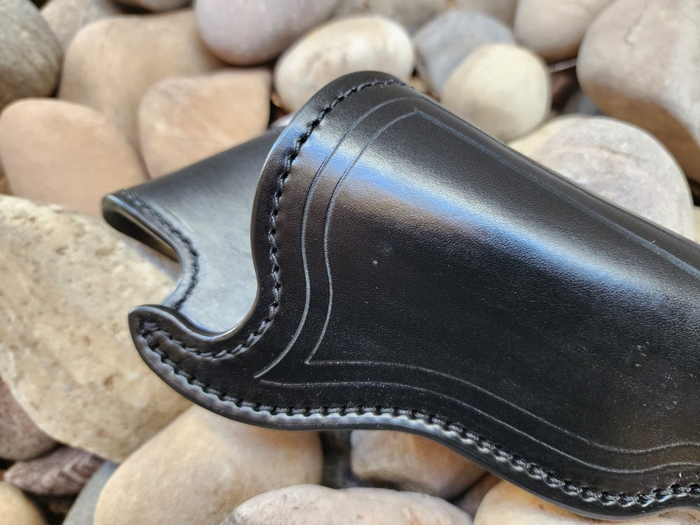 View of the mouth end of a black leather replica of wild bill hickoks holster. The holster sits on a bed of rocks.