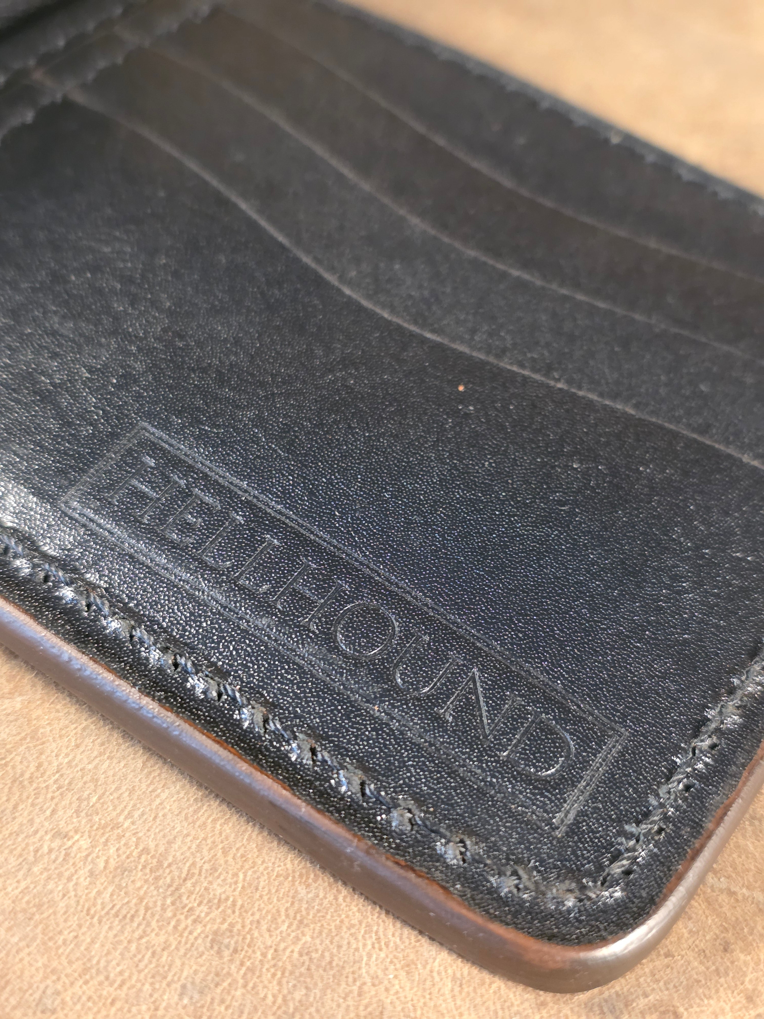A closeup image of the "hellhound" debossed logo in the lower corner of a wallet, pressed in black kanagroo leather.