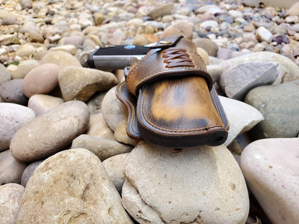 Muzzle end view of a rustic brown leather holster sitting on pale river rocks.