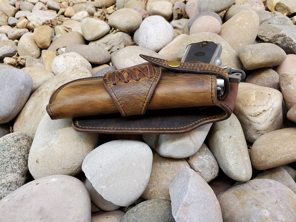 View of a 1911 leather holster sitting on pale river rocks with criss cross laces.