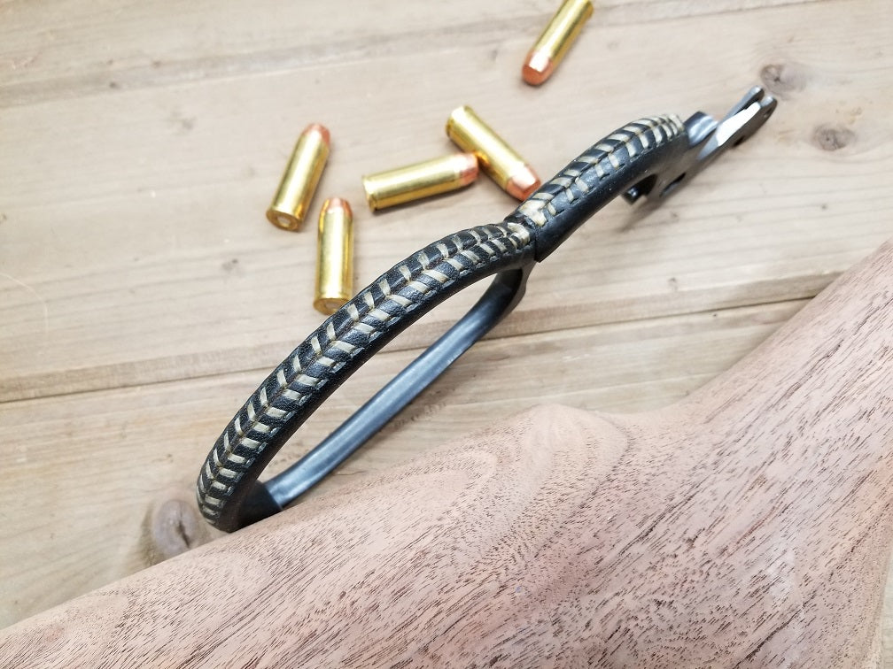 Black leather lever wrap with tan sinew stitched onto the lever from a lever action rifle next to five bullets.