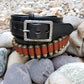 Black cowboy belt with hammered buckle coiled around itself sitting on smooth river rocks. 