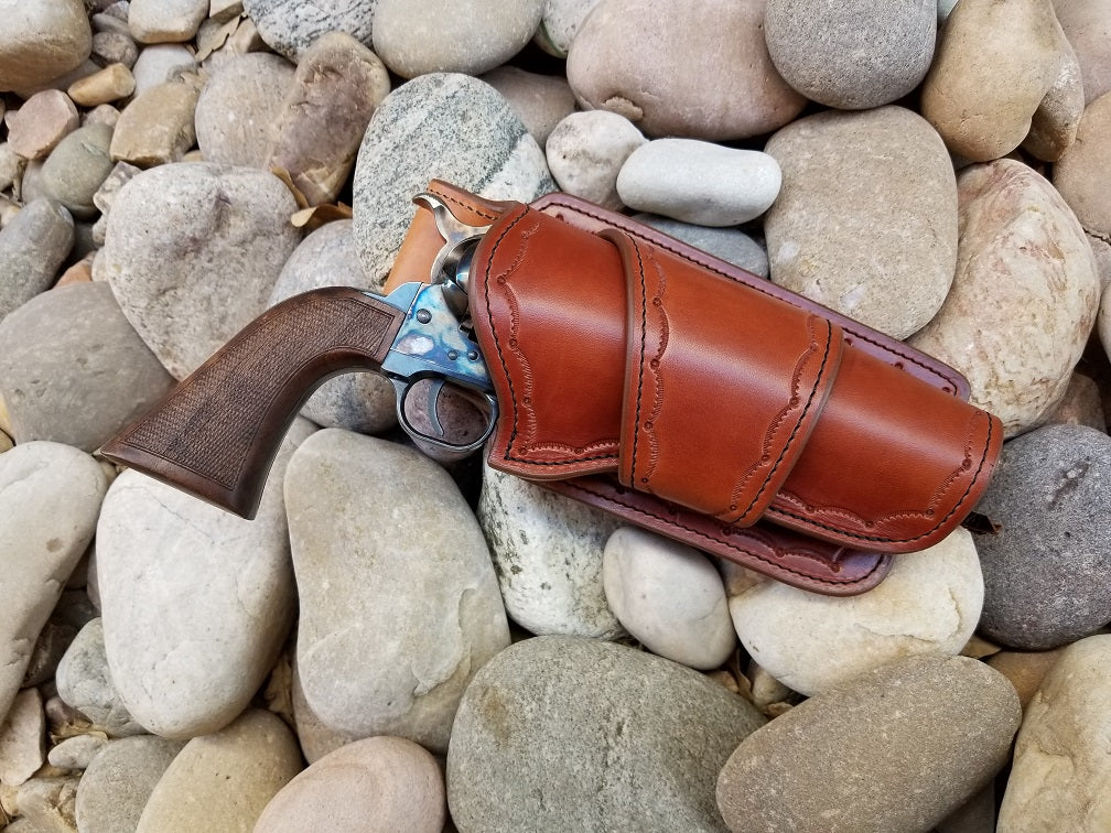 Western brown leather holster with a scallop tooled edge on bed light colored river rocks
