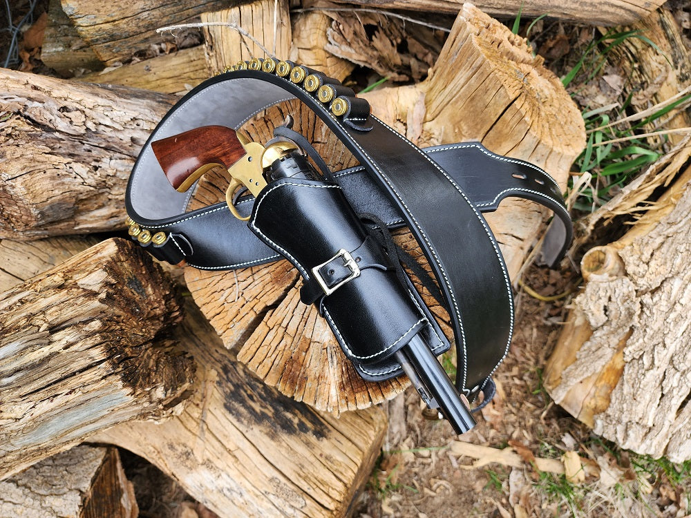 Angel Eyes inspired gun rig sitting on a log, the piece is made with black leather and a suede leather interior with white stitching and 24 bullet loops.