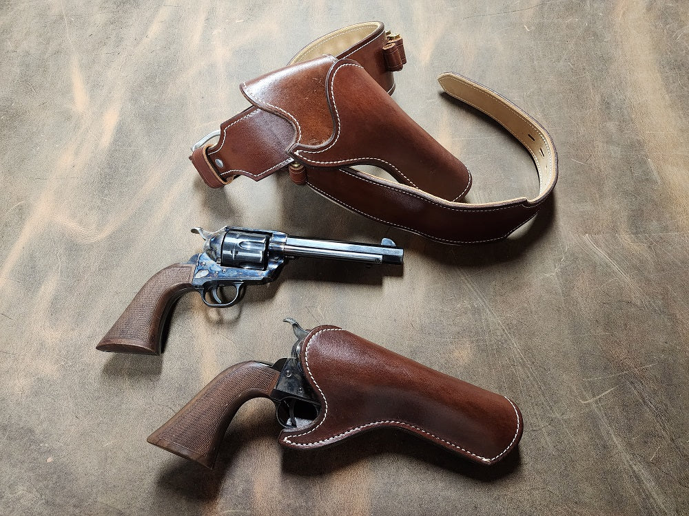 Brown leather gun rig curled on a ghostwood leather, just below the belt sits an old western revolver and another holstered just below.