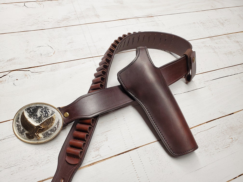 Brown leather lone wolf mcquade inspired holster and belt fitted with solid brass hardware and a gold and silver plated buckle. Brown leather bullet loops fit on the center of the belt. The rig is laying on white wooden slats.