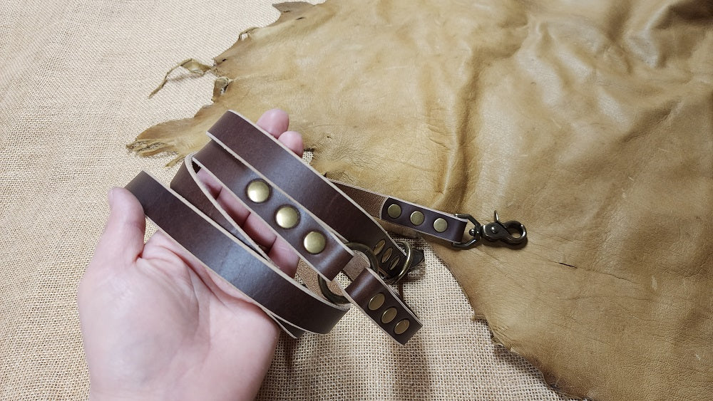 Coiled dark brown leather dog leash in a woman's hand against a burlap and goatskin background