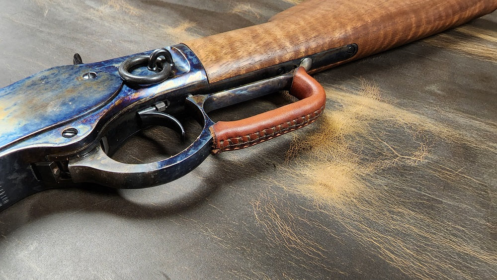 View from below lever action rifle with a brown leather wrap attached to the lever.