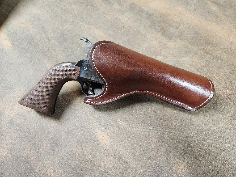 Brown leather holster with revolver sitting on a bed of ghost wood leather, the holster is stitched with white stitching.