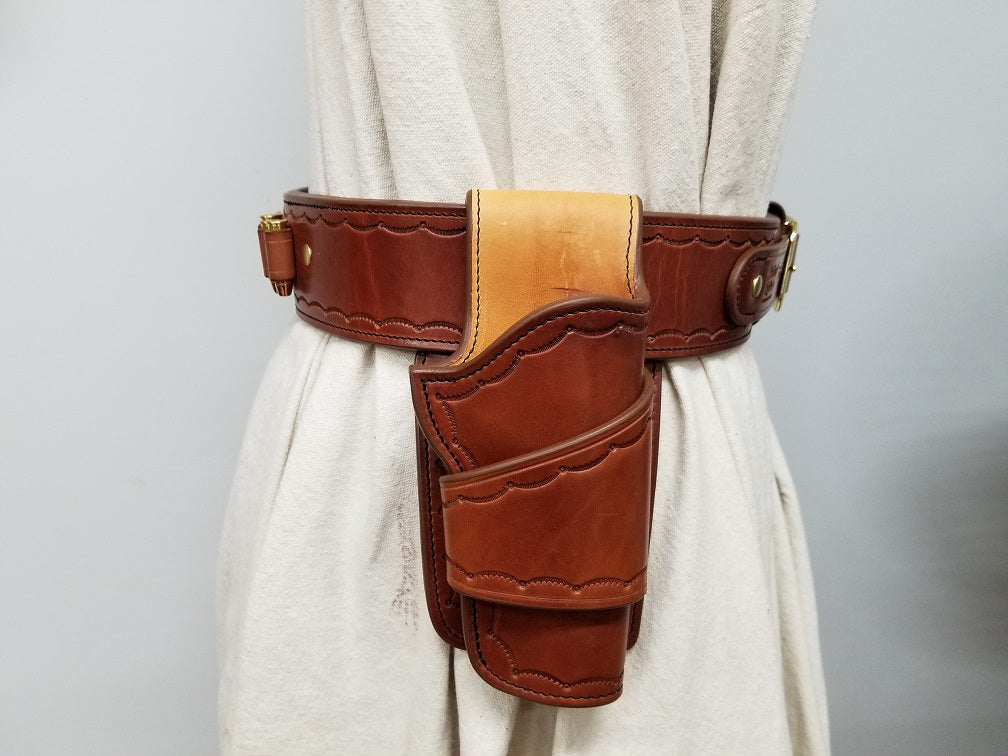 Side view of widow rock gun rig featuring the holster and bullet loops. The rig is made of brown leather with solid brass hardware and it tooled in a scallop pattern along the borders.