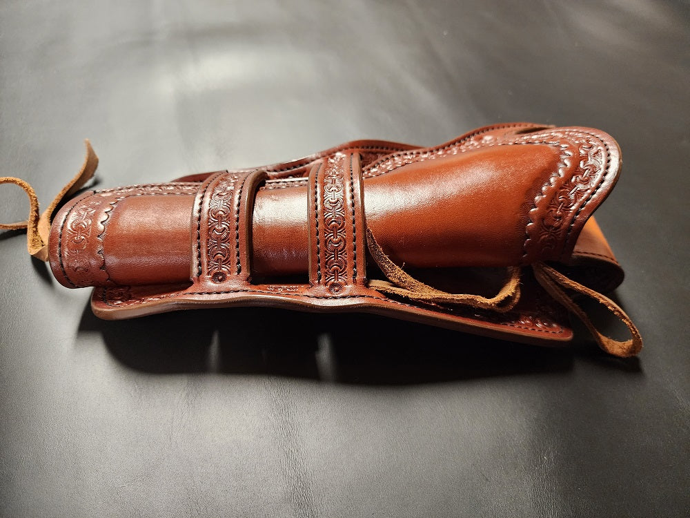 Brown leather intricately tooled leather holster with double Mexican loop collar, the holster is on a black leather background.