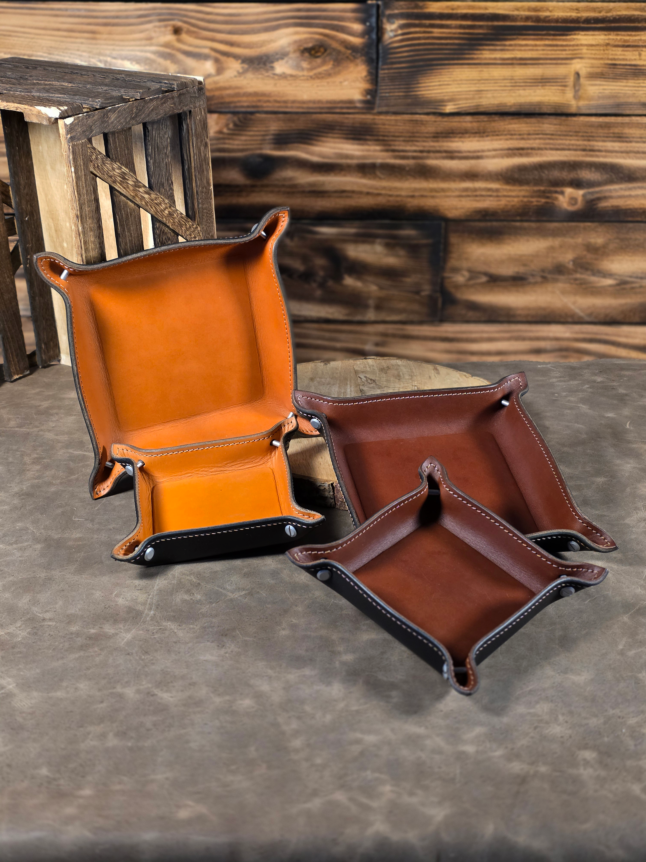 Four leather catch-all trays in brown and tan on a wooden surface.