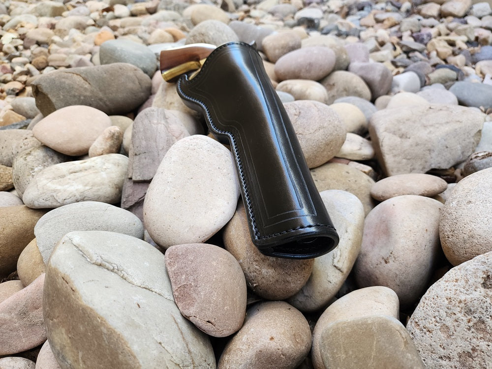 View of a black leather replica of Wild Bill Hickoks holster from the muzzle end. Holstered inside is a 1873 colt Peacemaker sitting on a bed of rocks.