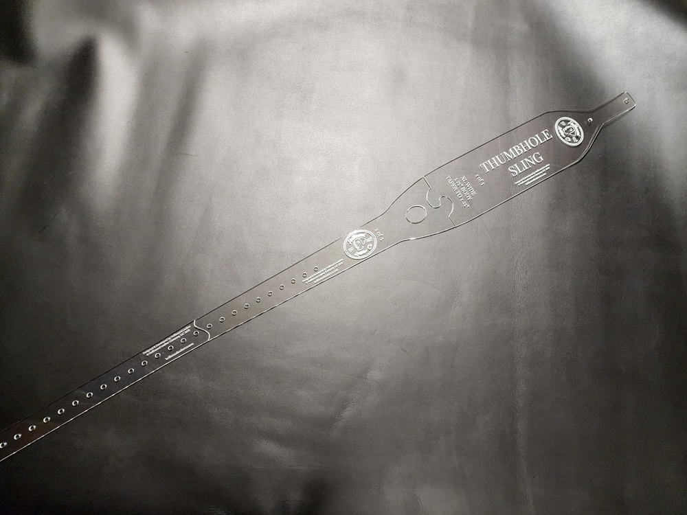 Extra wide thumbhole sling pattern, cut from clear plastic, sitting on a black background
