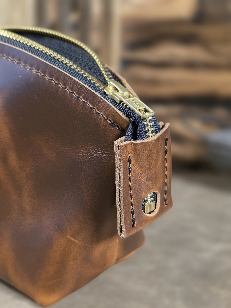 Close-up of a brown leather toiletry kit with a brass zipper.