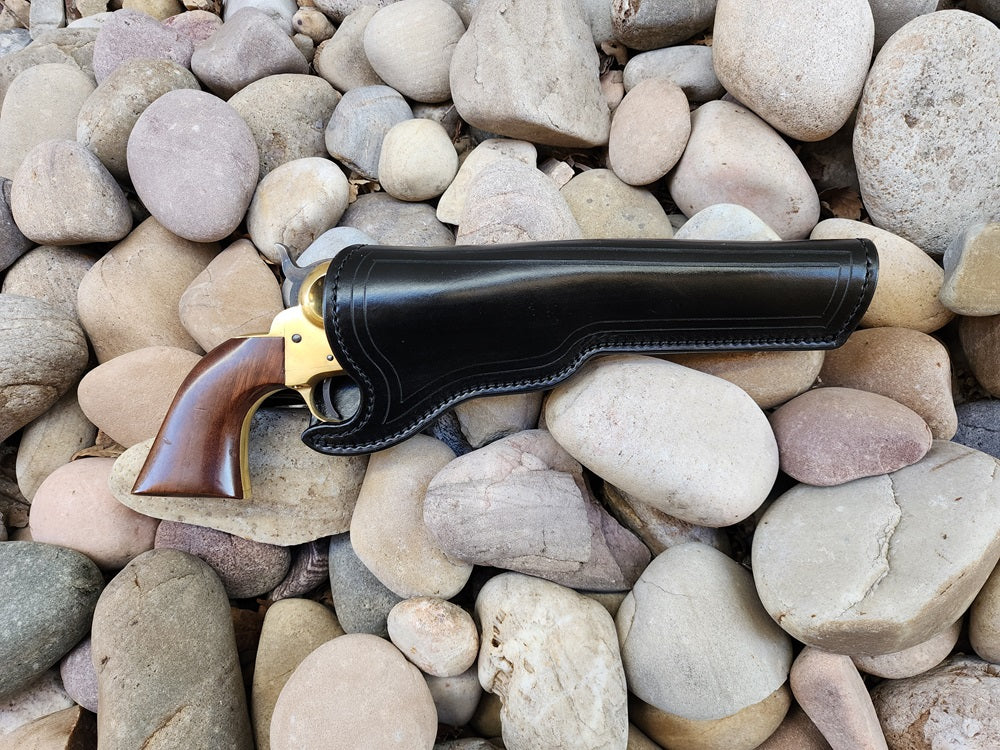 Tooled black leather holster sitting on a bed of river rocks, holstering a 1873 Colt Peacemaker.