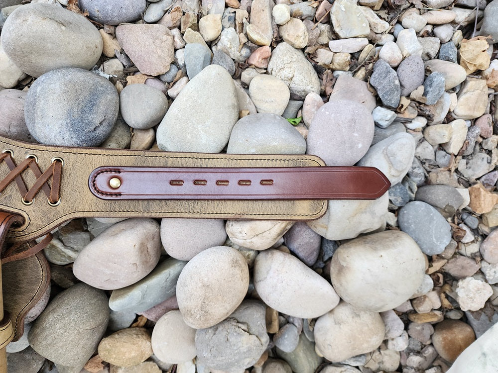 Buckle loop end of the double drop buscadero fitted with solid brass hardware laying on a bed of pale river rocks.