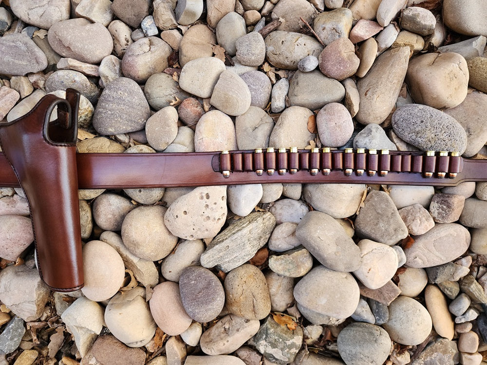 Lone Wolf Mcquade gun rig laying on a bed of river rocks focusing on the middle of the belt with the holster on the left hand of the frame and to the right showcases the bullet loops on the belt.
