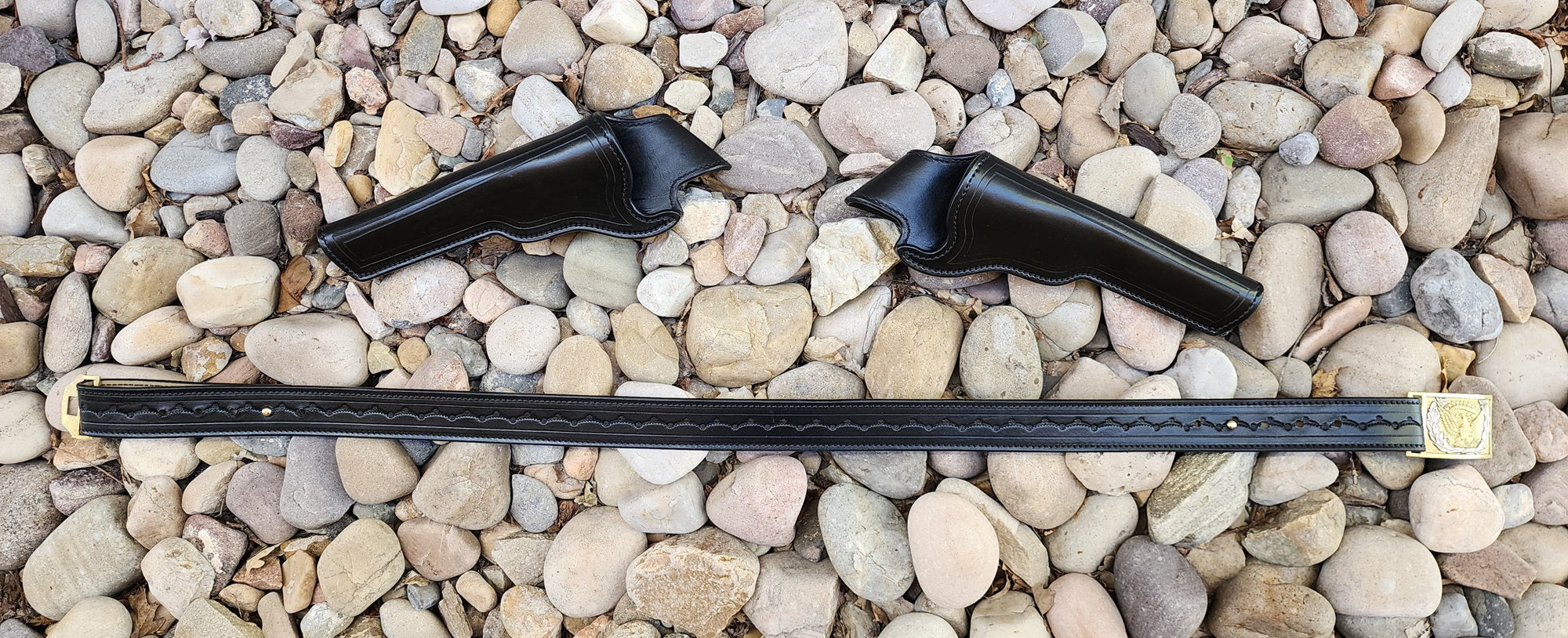 Holsters and belt from our replica of Wild Bill Hickok's gun rig layed on a bed of rocks, the holsters laying above the belt.