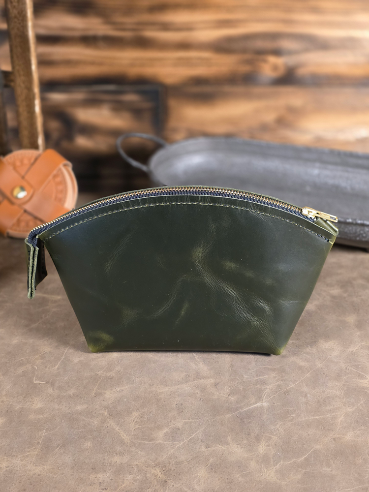 Green leather pouch with a solid brass zipper on a textured surface with blurred background
